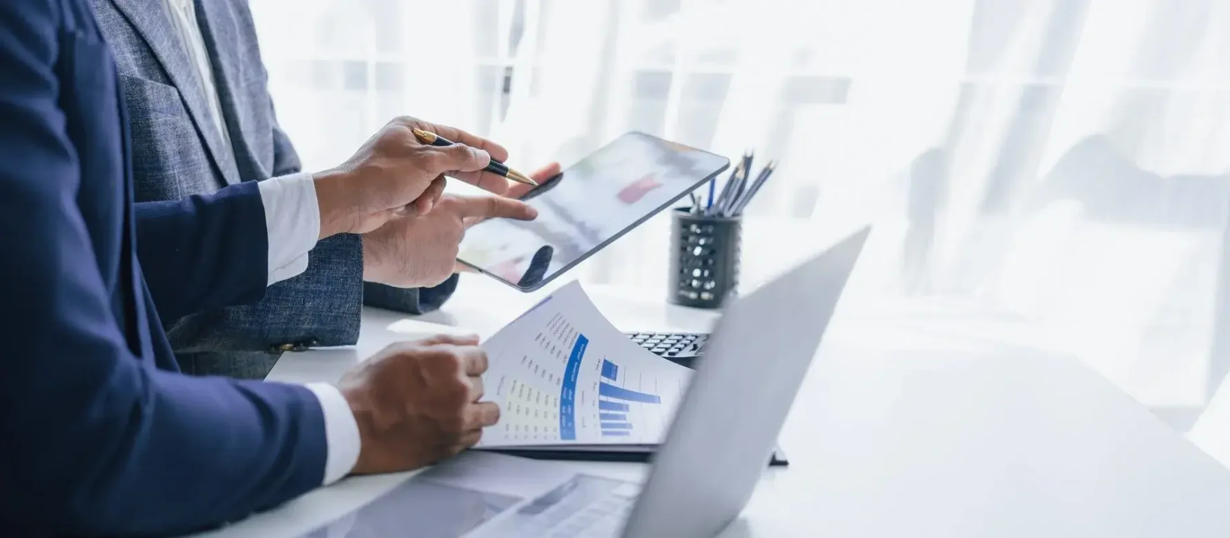 Gestores observan en una tablet mientras ojean unos documentos con gráficos